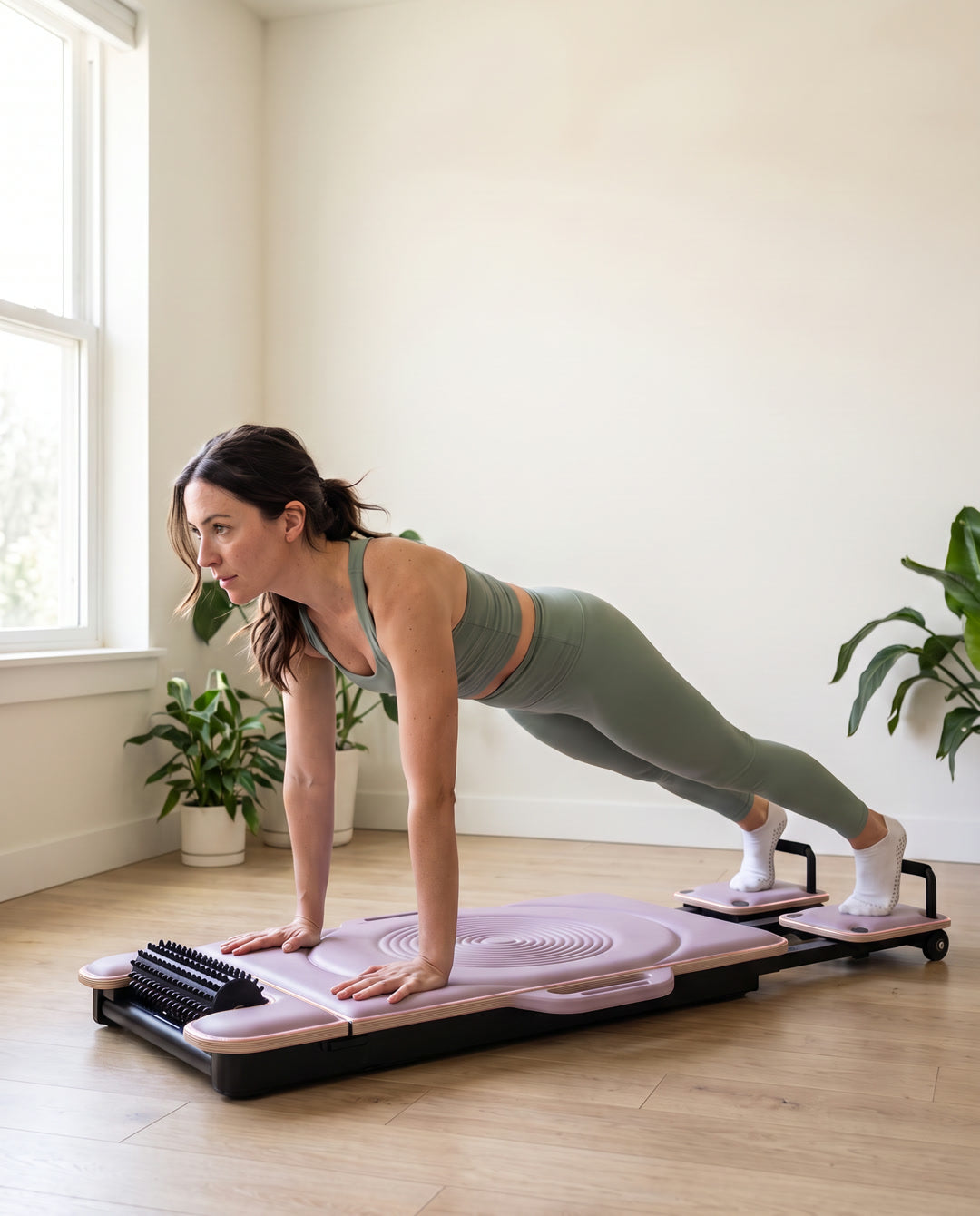 A woman in a light green sports set holding a plank with her hands on the lilac DROP-IN board and her feet on the sliding foot platforms.